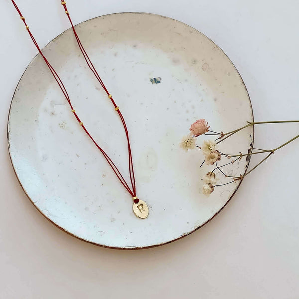 Delicate red thread necklace with gold accents and oval pendant on small plate.