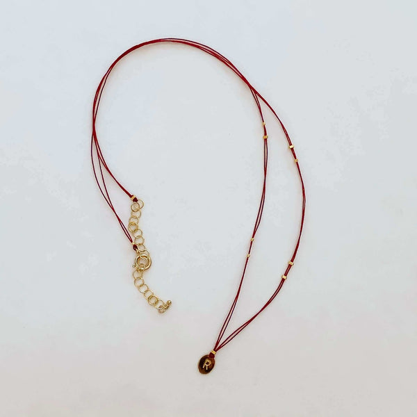 Delicate red thread necklace with gold accents and oval pendant.