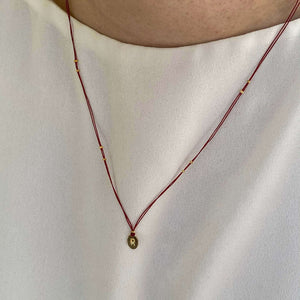 Woman wearing necklace red thread necklace with gold accents and oval pendant.
