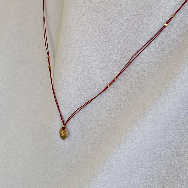 Woman wearing necklace red thread necklace with gold accents and oval pendant.