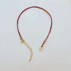 Delicate red thread necklace with gold accents and square pendant.