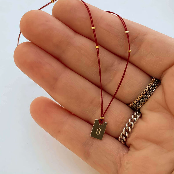 Close-up of fingers with delicate red thread necklace with gold accents and square pendant.