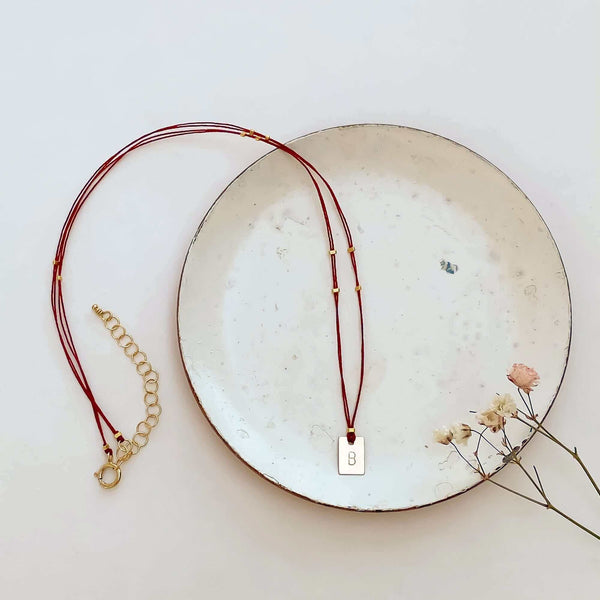 Delicate red thread necklace with gold accents and square pendant on small plate.