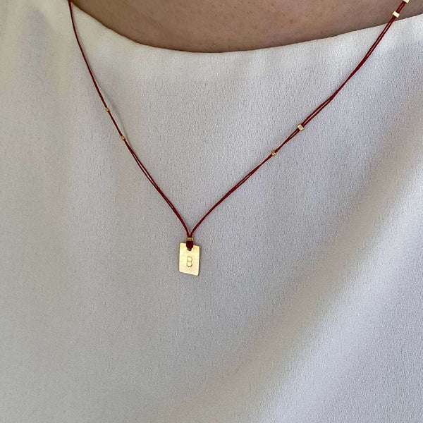 Woman wearing necklace red thread necklace with gold accents and square pendant.