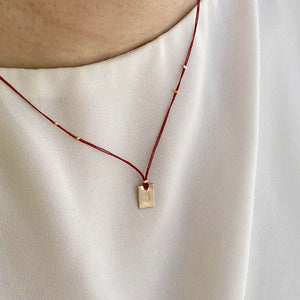 Woman wearing necklace red thread necklace with gold accents and square pendant.