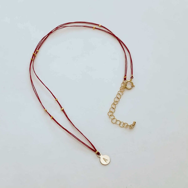 Delicate red thread necklace with gold accents and round pendant.