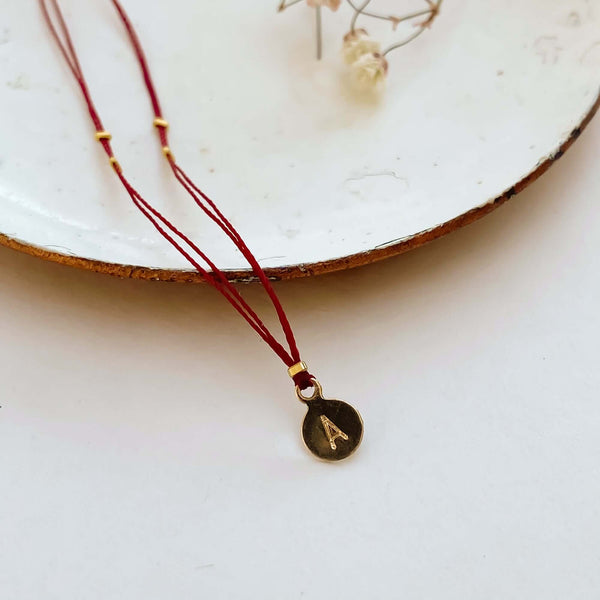 Close-up of delicate red thread necklace with gold accents and round pendant on small plate.