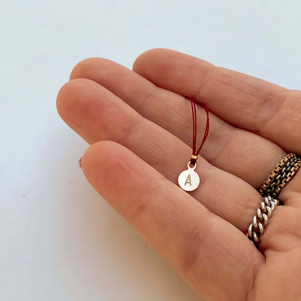 Close-up of fingers with delicate red thread necklace with gold accents and round pendant.
