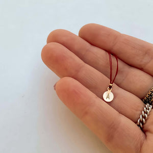 Close-up of fingers with delicate red thread necklace with gold accents and round pendant.