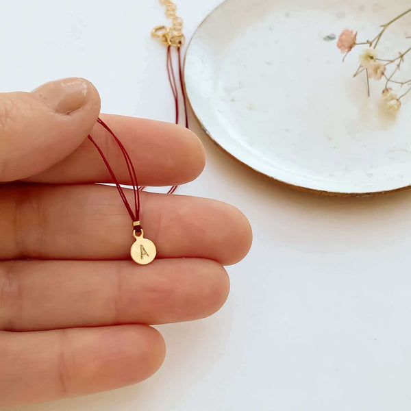 Close-up of fingers with delicate red thread necklace with gold accents and round pendant with small plate.