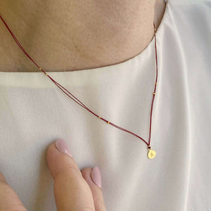 Woman wearing necklace red thread necklace with gold accents and round pendant.