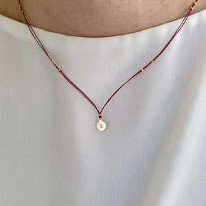 Woman wearing necklace red thread necklace with gold accents and round pendant.