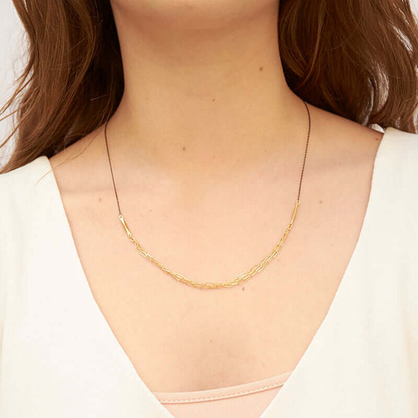 Woman wearing a black chain necklace with 3 delicate elongated link chains at the front.