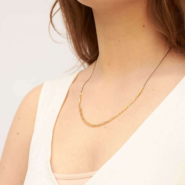 Woman wearing a black chain necklace with 3 delicate elongated link chains at the front, shown side angle.