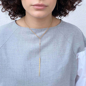 Woman wearing delicate long gold necklace with elongated thin feather pendant, worn short.