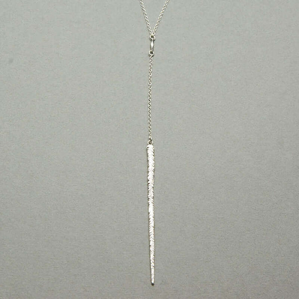 Close-up delicate long silver necklace with elongated thin feather pendant.