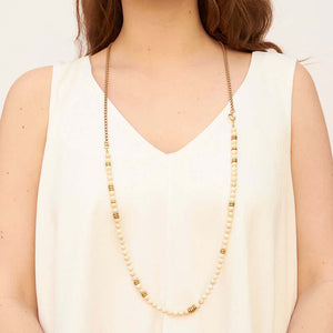Woman wearing necklace of chunky gold chain with white river stones and brass beads.