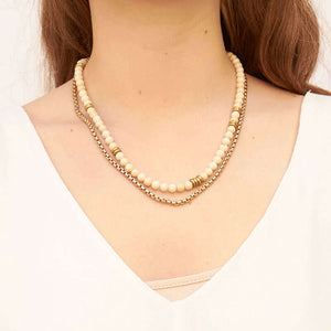 Woman wearing necklace of chunky gold chain with white river stones and brass beads, worn doubled.