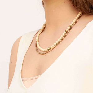 Woman wearing necklace of chunky gold chain with white river stones and brass beads, worn doubled, shown side angle.
