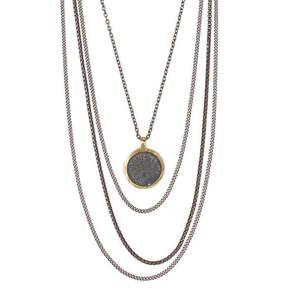 Close-up of dark multi-chain necklace with round coin shaped etched brass pendant.