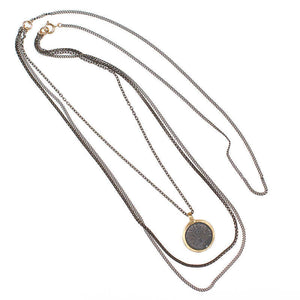 Dark multi-chain necklace with round coin shaped etched brass pendant.