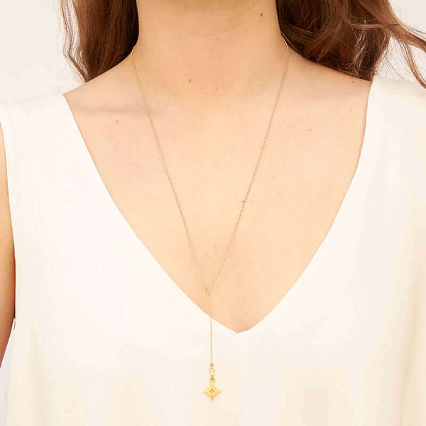 Woman wearing gold bead chain necklace with small geometric cross shaped pendant and slider.