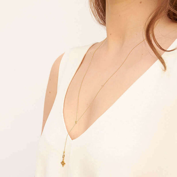 Woman wearing gold bead chain necklace with small geometric cross shaped pendant and slider, shown side angle.