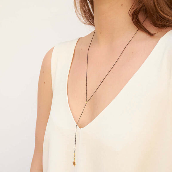 Woman wearing dark bead chain necklace with small geometric cross shaped pendant and slider, shown side angle.