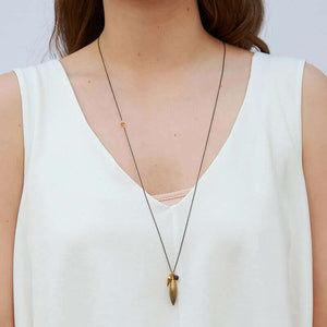 Woman wearing dark chain necklace with pendant of large brass spike and small gold spike and garnet.