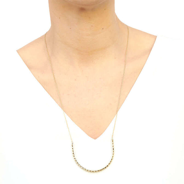 Woman wearing gold necklace with large curved beaded bar pendant.
