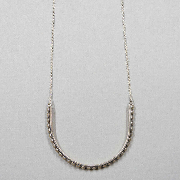 Close-up of silver necklace with large curved beaded bar pendant.