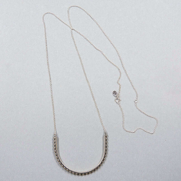 Silver necklace with large curved beaded bar pendant.