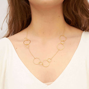 Woman wearing a gold necklace, groups of gold hoops on gold chain.