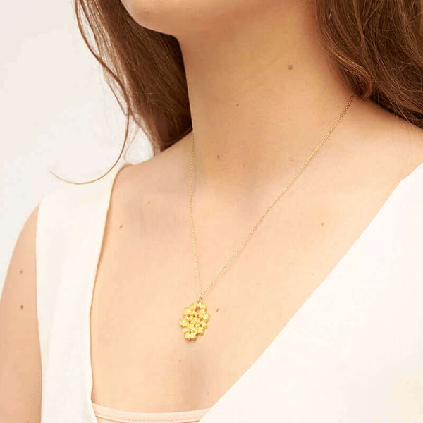 Woman wearing a gold chain necklace with cast gold tree canopy inspired pendant, shown side angle.