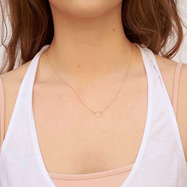 Woman wearing a delicate gold chain necklace with a simple circle pendant.