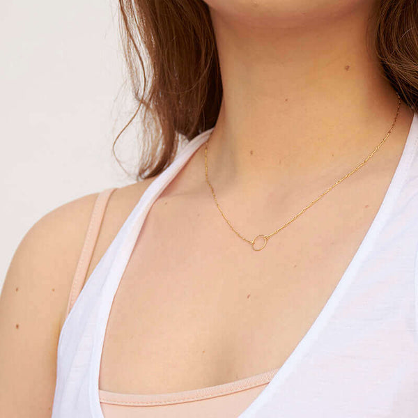 Woman wearing a delicate gold chain necklace with a simple circle pendant, shown side angle.