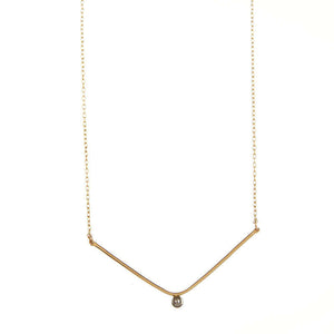 Close-up of delicate gold chain necklace, wide v pendant with dark pearl in middle.