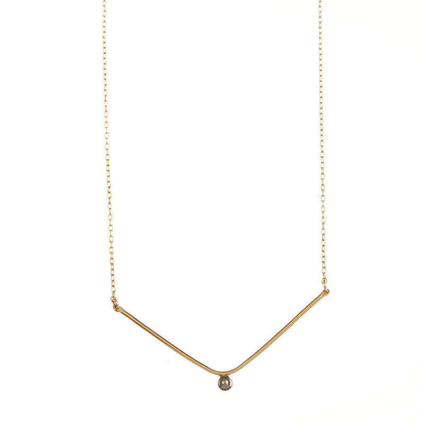 Close-up of delicate gold chain necklace, wide v pendant with dark pearl in middle.