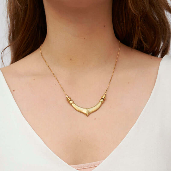 Woman wearing a delicate gold chain necklace with chunky hand cast organic curved pendant.