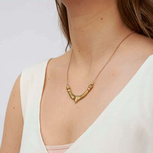 Woman wearing a delicate gold chain necklace with chunky hand cast organic curved pendant, shown side angle.