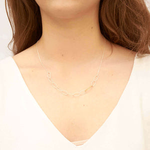 Woman wearing a silver chain necklace with wide oval links in front with detail on 2 gold links.
