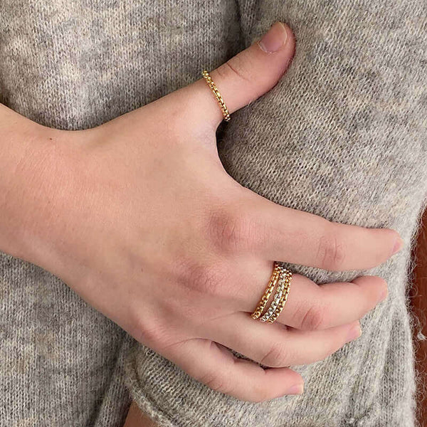 Close-up of hand wearing assorted thick silver and gold chain rings.