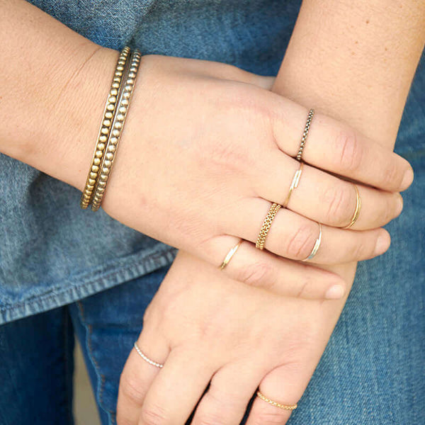 Close-up of hand wearing various gold and silver hand-hammered and chain rings.
